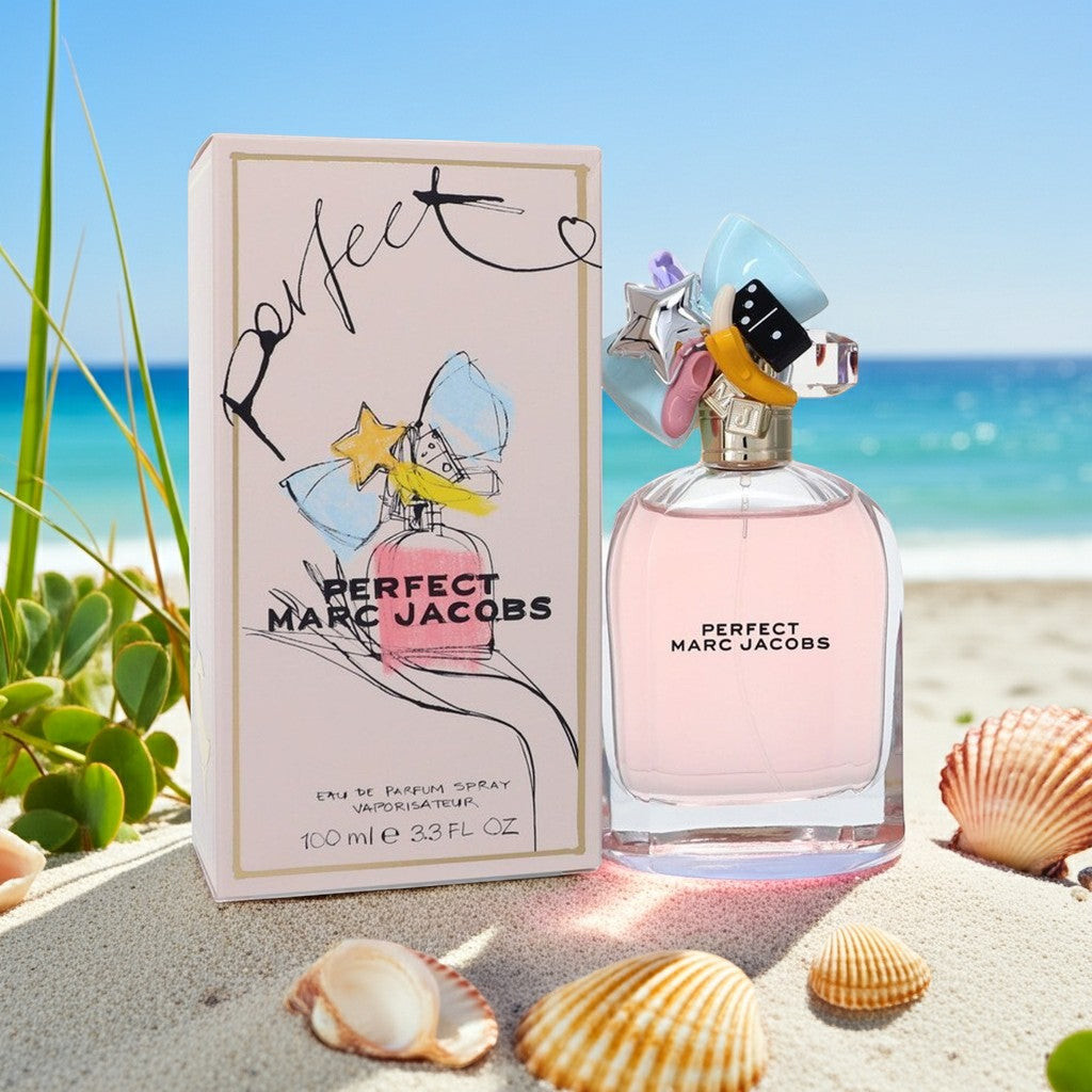 AuraGlow Marc Jacobs Perfect Eau De Parfum bottle and box on a sandy beach with seashells and ocean background